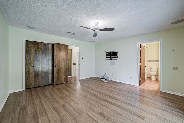 unfurnished bedroom featuring a closet, light hardwood / wood-style flooring, ensuite bathroom, a textured ceiling, and ceiling fan