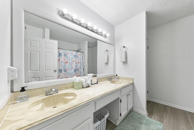 7600 Seawall Blvd Unit 115, Galveston, TX 77551 - bathroom featuring wood finished floors, baseboards, double vanity, a shower with curtain, and a textured ceiling