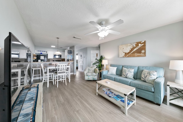 living room with a textured ceiling, light hardwood / wood-style floors, and ceiling fan