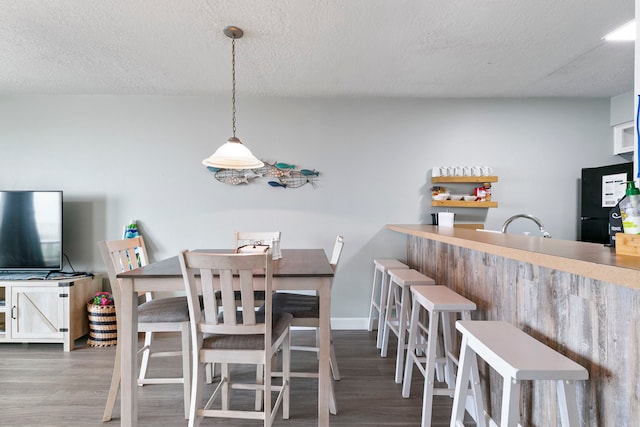 dining area with dark wood-type flooring, a textured ceiling, and bar area