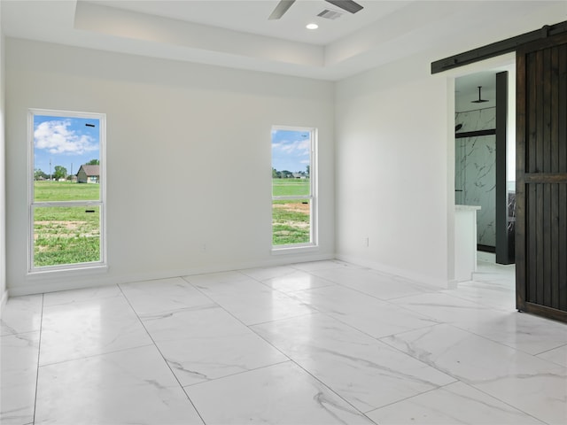 empty room featuring a barn door, a tray ceiling, and ceiling fan