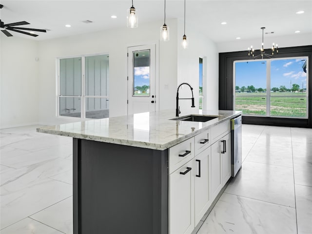 kitchen with light stone countertops, sink, pendant lighting, white cabinets, and a kitchen island with sink