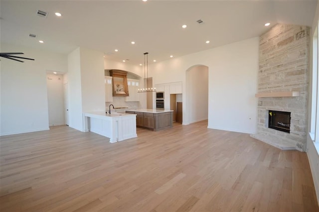 kitchen with light wood finished floors, appliances with stainless steel finishes, open floor plan, a stone fireplace, and a sink