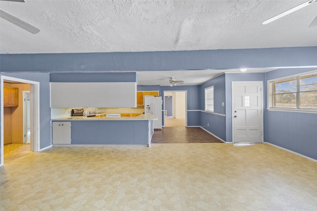 kitchen with a breakfast bar, ceiling fan, white fridge with ice dispenser, and a textured ceiling