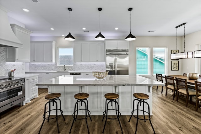 kitchen with light wood-type flooring, a large island, custom range hood, and high end appliances