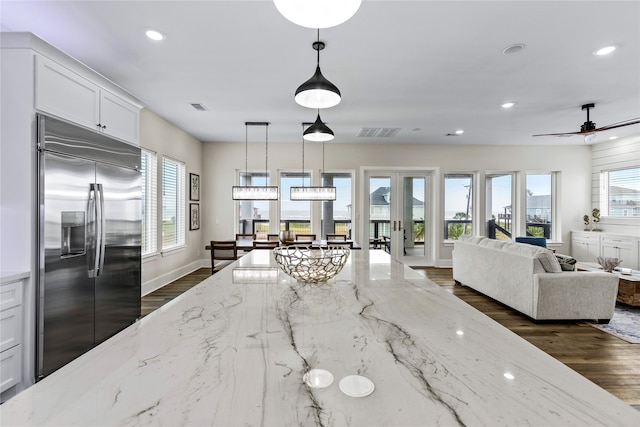 kitchen featuring stainless steel built in fridge, white cabinetry, dark hardwood / wood-style floors, light stone countertops, and hanging light fixtures