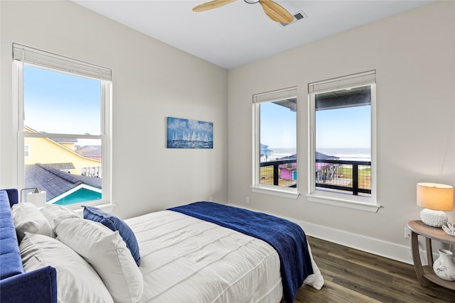 bedroom with a water view, dark wood-type flooring, multiple windows, and ceiling fan