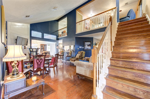 stairway with hardwood / wood-style floors, high vaulted ceiling, and a textured ceiling