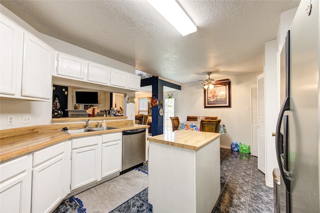 kitchen with appliances with stainless steel finishes, a textured ceiling, wooden counters, and white cabinets