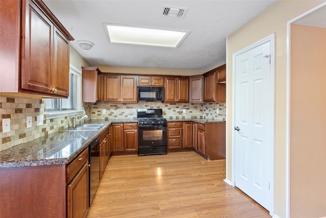 kitchen featuring stone counters, tasteful backsplash, black appliances, and light wood-type flooring