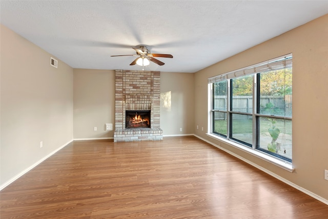 unfurnished living room featuring ceiling fan, a textured ceiling, light hardwood / wood-style flooring, and a brick fireplace