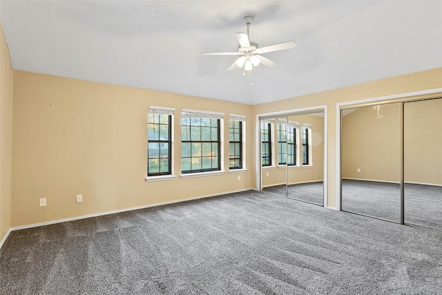 unfurnished bedroom featuring ceiling fan, dark colored carpet, and two closets