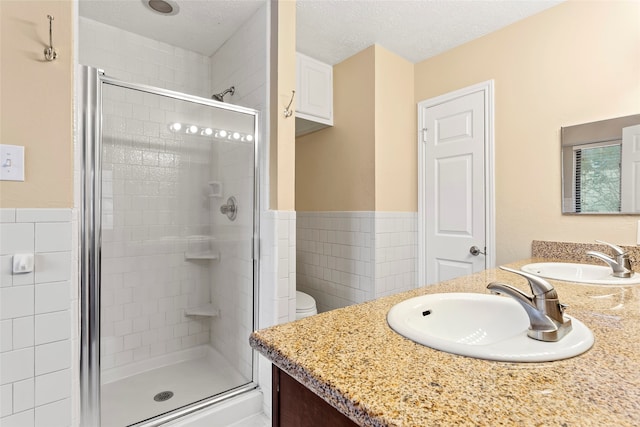 bathroom with toilet, a shower with shower door, vanity, tile walls, and a textured ceiling