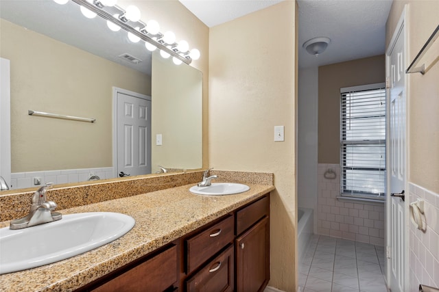 bathroom with tile patterned flooring, a washtub, vanity, tile walls, and a textured ceiling