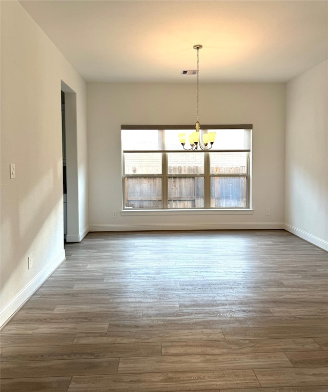 spare room featuring an inviting chandelier, baseboards, a wealth of natural light, and wood finished floors