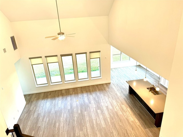 additional living space with light wood-type flooring, a high ceiling, baseboards, and a ceiling fan