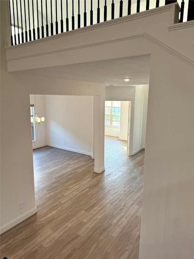 spare room featuring a chandelier, baseboards, and light wood finished floors