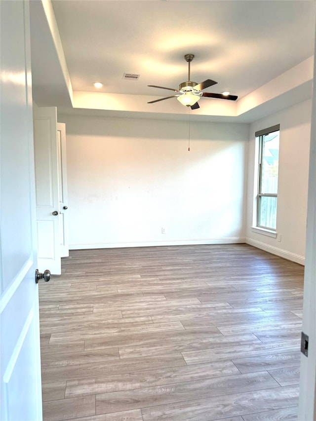 empty room with visible vents, baseboards, ceiling fan, a tray ceiling, and light wood-type flooring