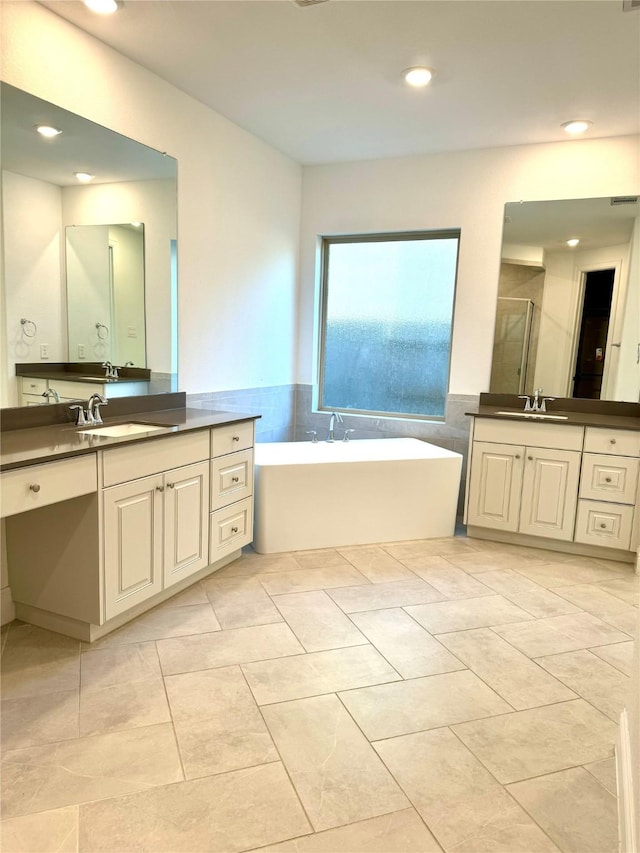 full bath featuring a freestanding tub, two vanities, a sink, and a shower stall