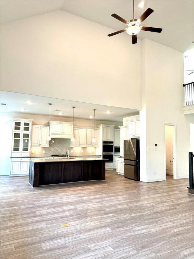 kitchen with stainless steel appliances, light countertops, tasteful backsplash, an island with sink, and decorative light fixtures