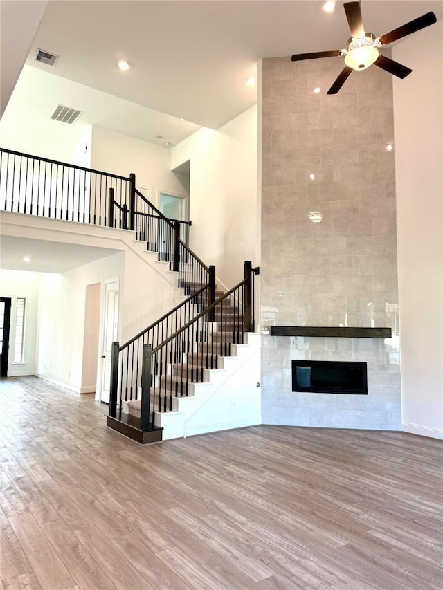 unfurnished living room with visible vents, a tiled fireplace, a towering ceiling, wood finished floors, and stairs