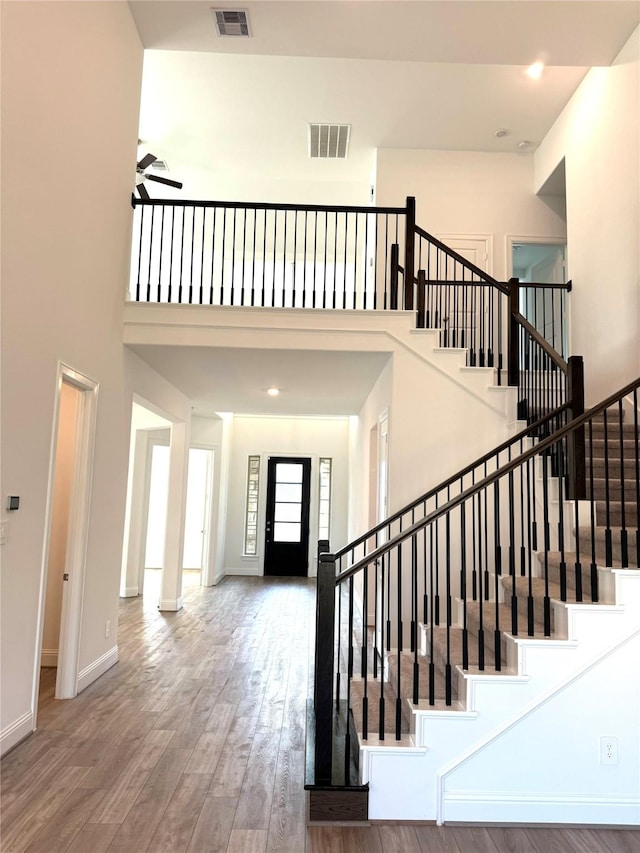 stairs with visible vents, a towering ceiling, baseboards, and wood finished floors