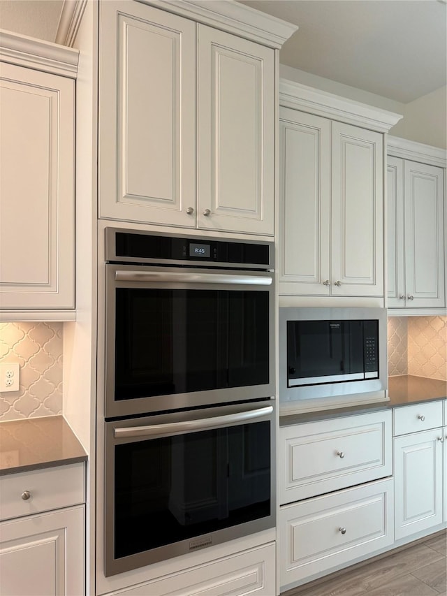 kitchen with white cabinets, black microwave, backsplash, and stainless steel double oven