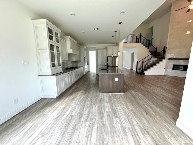 kitchen featuring pendant lighting, dark countertops, glass insert cabinets, freestanding refrigerator, and a kitchen island with sink