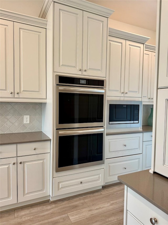 kitchen featuring decorative backsplash, dark countertops, light wood-style flooring, built in microwave, and stainless steel double oven