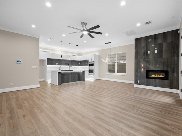 unfurnished living room with ceiling fan, light hardwood / wood-style floors, sink, and a fireplace