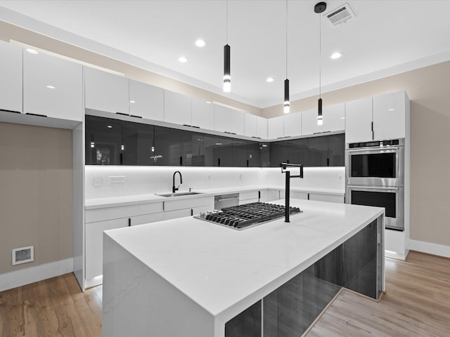 kitchen with pendant lighting, appliances with stainless steel finishes, sink, white cabinetry, and a center island with sink