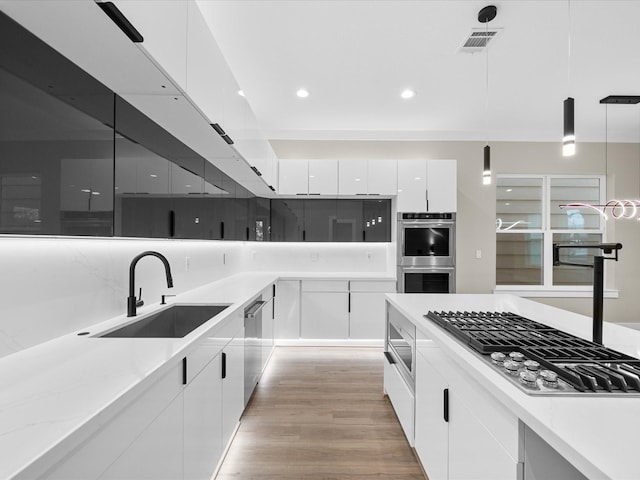 kitchen featuring sink, stainless steel appliances, hanging light fixtures, and white cabinets