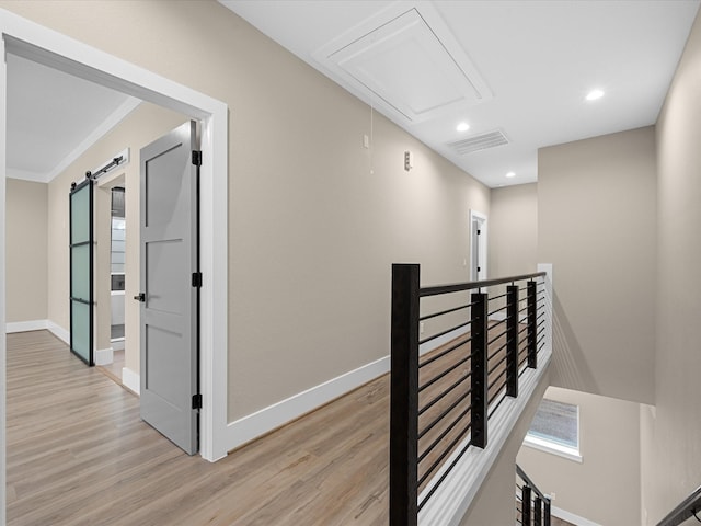 hall with a barn door, ornamental molding, and light hardwood / wood-style floors