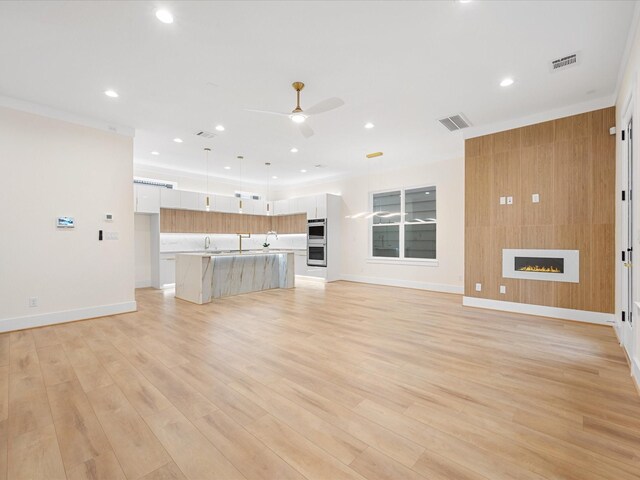 unfurnished living room with ceiling fan, sink, a large fireplace, and light wood-type flooring