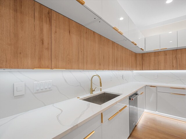 kitchen featuring dishwasher, white cabinetry, sink, light stone counters, and light hardwood / wood-style flooring