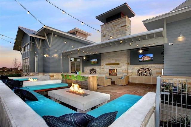 patio terrace at dusk featuring a hot tub, an outdoor living space with a fire pit, and a deck