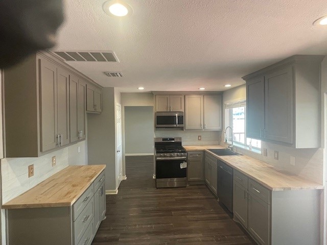 kitchen with wooden counters, gray cabinetry, sink, appliances with stainless steel finishes, and dark hardwood / wood-style flooring