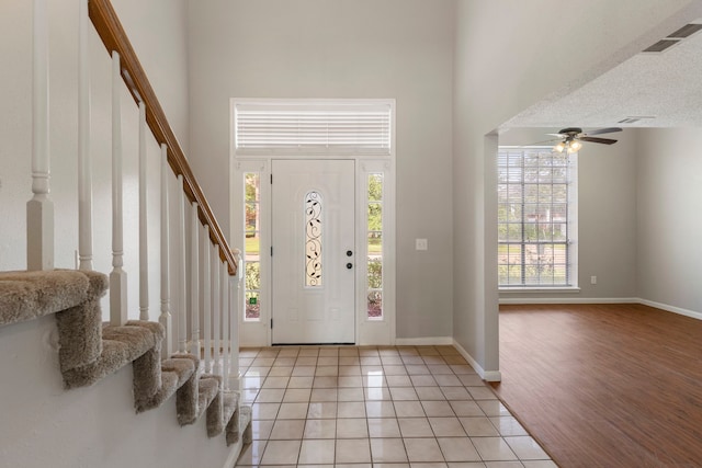 entrance foyer featuring a towering ceiling, ceiling fan, a textured ceiling, and light wood-type flooring