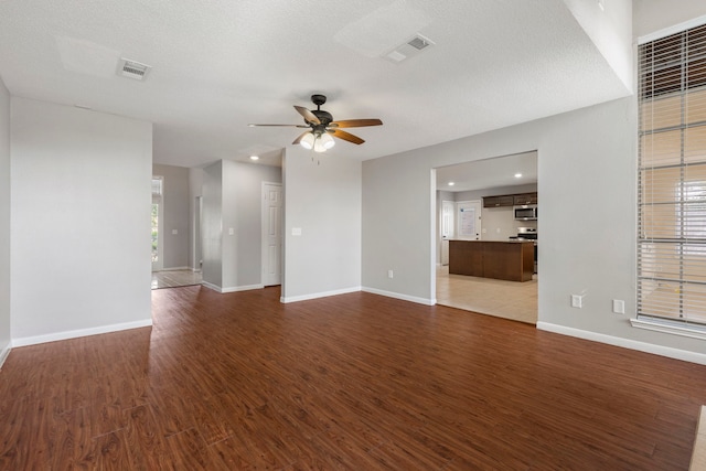 unfurnished living room featuring ceiling fan, a textured ceiling, and dark hardwood / wood-style flooring