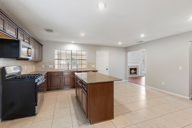 kitchen featuring light tile patterned flooring, light stone counters, a kitchen island, black gas stove, and decorative backsplash