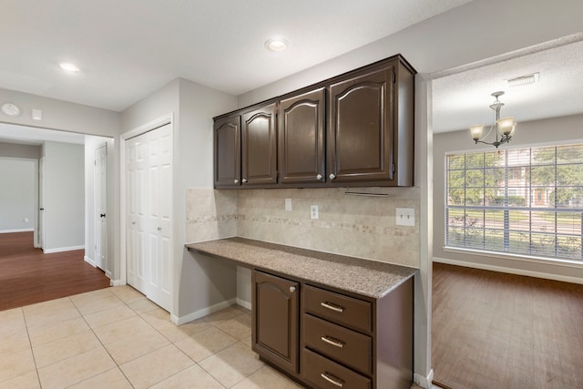 kitchen featuring light hardwood / wood-style floors, an inviting chandelier, dark brown cabinetry, hanging light fixtures, and backsplash