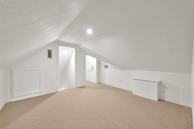 bonus room featuring light carpet, lofted ceiling, and a textured ceiling