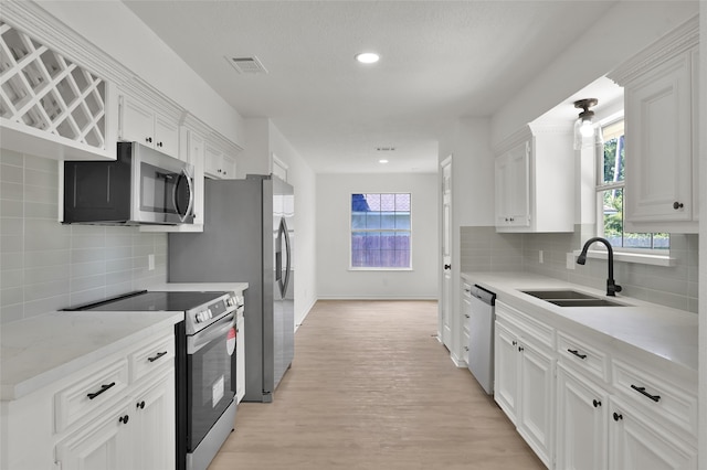 kitchen with light hardwood / wood-style flooring, backsplash, sink, white cabinetry, and appliances with stainless steel finishes