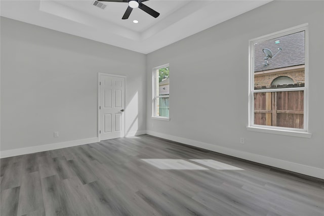 spare room with ceiling fan, a tray ceiling, and light wood-type flooring