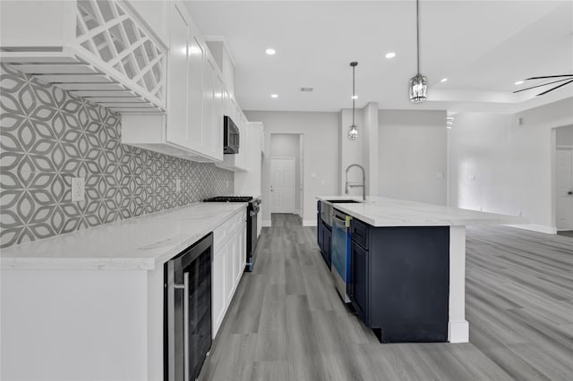 kitchen with stainless steel appliances, pendant lighting, white cabinets, wine cooler, and a center island with sink