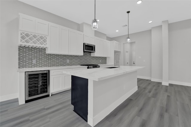 kitchen with an island with sink, white cabinetry, stainless steel appliances, decorative light fixtures, and beverage cooler