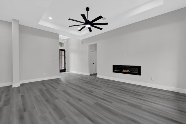 unfurnished living room with hardwood / wood-style floors, ceiling fan, and a raised ceiling