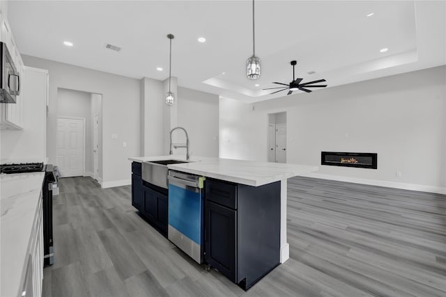 kitchen with a kitchen island with sink, stainless steel appliances, sink, decorative light fixtures, and white cabinets