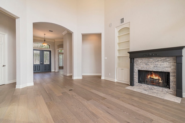 unfurnished living room featuring french doors, a fireplace, wood-type flooring, ornamental molding, and built in shelves