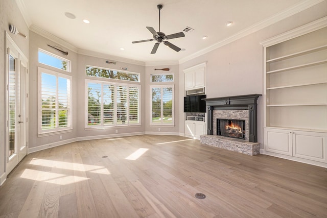 unfurnished living room with a stone fireplace, crown molding, light wood-type flooring, and ceiling fan